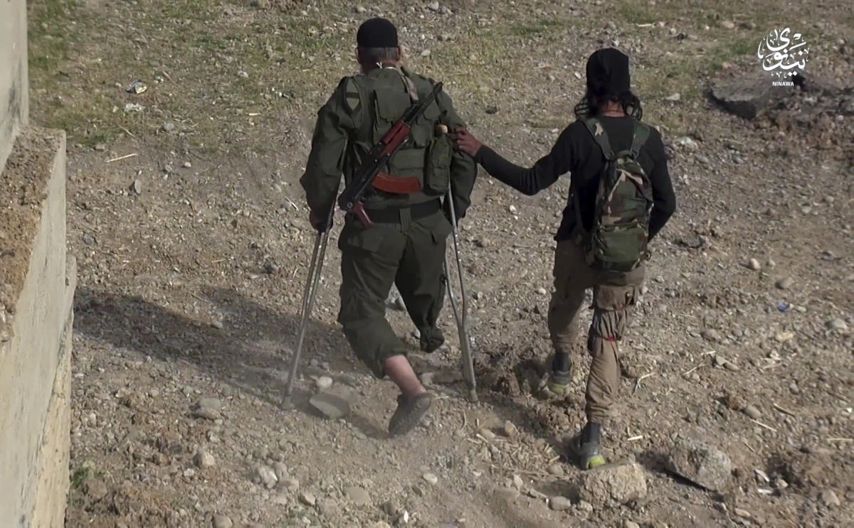 This undated frame grab from video posted online on May 17 by Daesh shows Abu Shuaib Al-Maslawi, left, as he hops on his left leg with the help of crutches and a Daesh militant on his way to detonate himself amid Iraqi troops in the northern city of Mosul, Iraq. (AP)