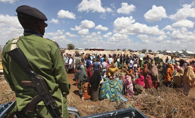A Somali policeman provides security as displaced Somalis gather outside their makeshift shelters at a camp in Baidoa, Somalia. At least 14 people, most of them civilians, were killed Friday, June 9, 2017 as soldiers clashed over food aid in drought-ravaged Somalia's southwestern city of Baidoa, where tens of thousands of people have streamed in seeking assistance. (AP Photo/Farah Abdi Warsameh, file)