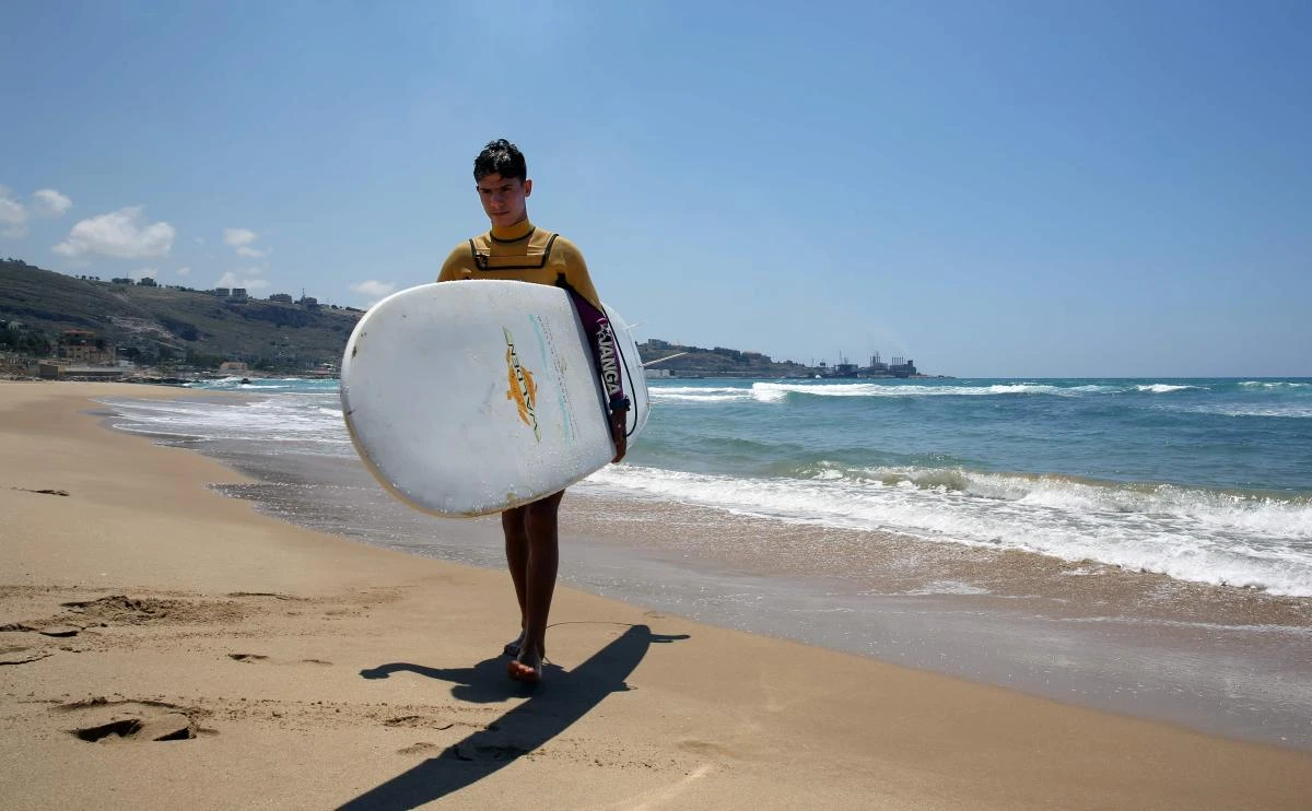 Ali Kassem, a 17-year-old Syrian refugee, carries his surfboard on a beach in the town of Jiyeh, south of the Lebanese capital Beirut. (AFP)