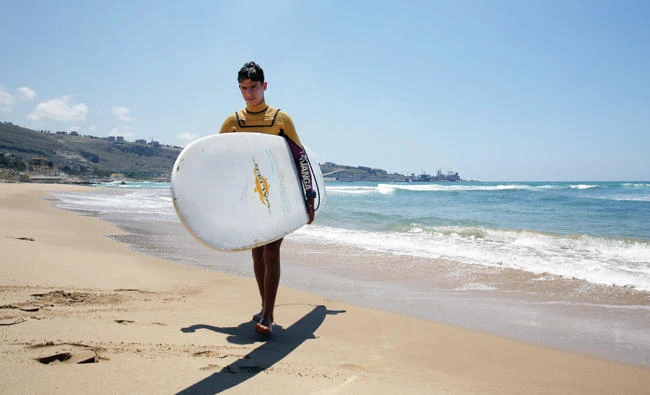 Ali Kassem carries his surfboard on a beach in Jiyeh, Lebanon. (AFP)