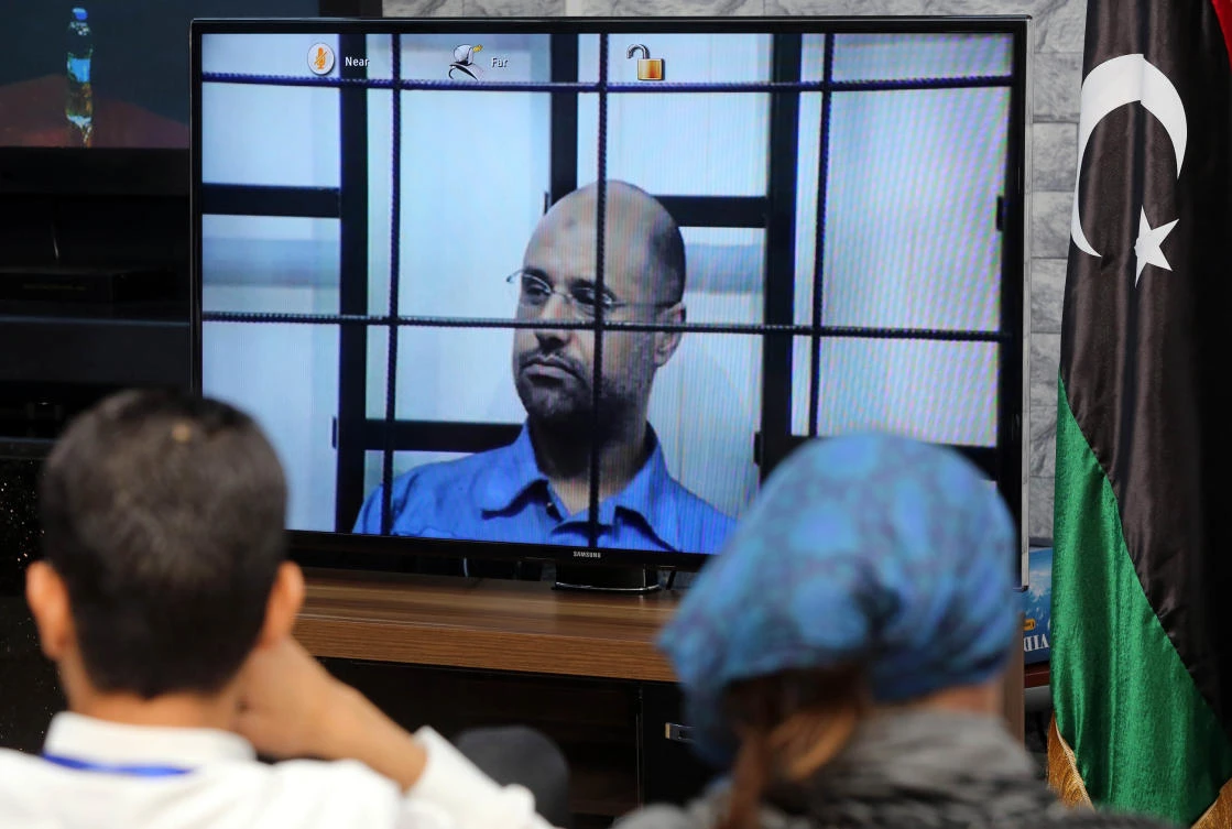 This file photo taken on April 27, 2014 shows journalists watching as the judges (unseen), question Seif al-Islam (C), the son of slain Libyan dictator Muammar Qaddafi, broadcasted live from the western Libyan city of Zintan, from inside a room in Tripoli. (AFP / MAHMUD TURKIA)