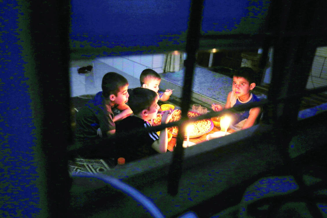 A Palestinian family eats dinner by candlelight at their makeshift home in the Rafah refugee camp, in the southern Gaza Strip, during a power outage on Sunday. (AFP)