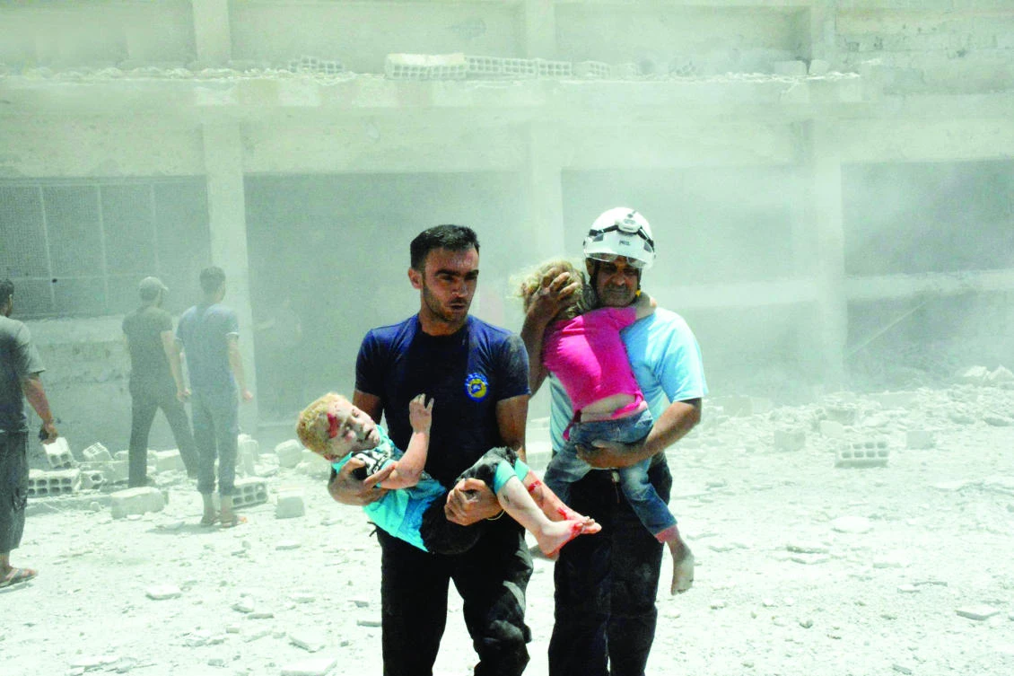 Civil Defense workers carrying children after airstrikes hit a school housing a number of displaced people, in the western part of the southern Daraa province of Syria, on Wednesday. (AP)