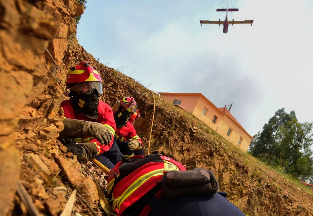 Some firefighters protect themselves as a firefighting plane drops its load on a wildfire in Vale da Ponte, Pedrograo Grande. (AFP)