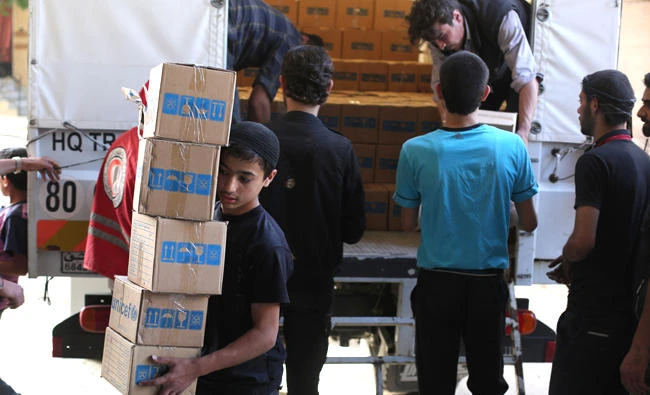 Syrians unload boxes of aid donated by UNHCR in the opposition-held and besieged town of Harasta, in the Eastern Ghouta region outside Damascus, on Monday. (AFP)