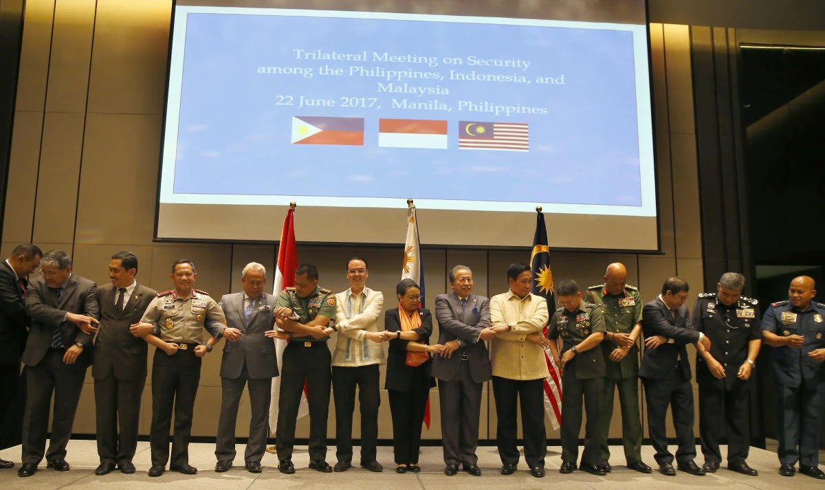 Philippines Alan Peter Cayetano (seventh from left), Indonesian Retno Marsudi (eight from left), Malaysia's Anifah Haji Aman (ninth from left), as well as their respective armed forces and police chiefs, link arms prior to the start of their Trilateral Security Meeting in suburban Pasay city southeast of Manila on Thursday. (AP)