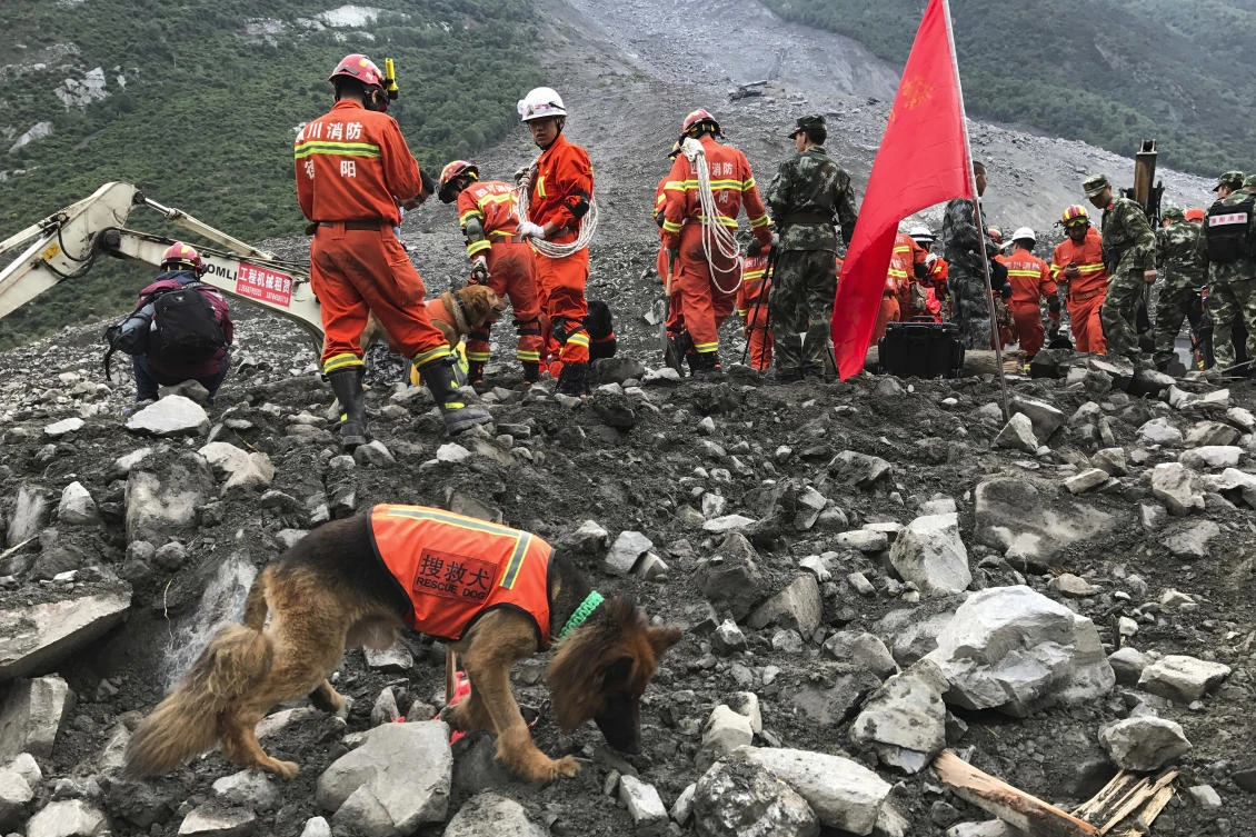 Rescuers with sniffer dogs stand near an earthmoving equipment digging at the site of a landslide in Xinmo village in Maoxian County in southwestern China's Sichuan Province, Sunday, June 25, 2017. Crews searching through the rubble left by a landslide that buried a mountain village under tons of soil and rocks in southwestern China on Saturday found bodies, but more than 100 people remained missing. (AP)