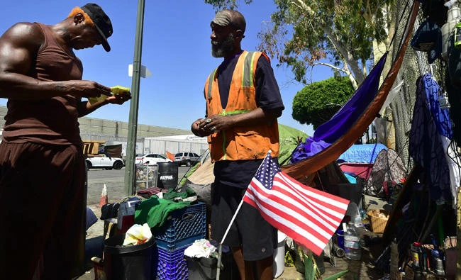 Homeless veteran Kendrick Bailey (C) has General Dogon (L) looks over some citations he recently received outside his tent on a streetcorner near Skid Row in downtown Los Angeles, California on June 20, 2017. (AFP / FREDERIC J. BROWN)