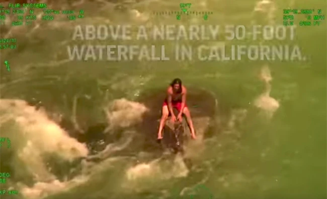 Kalani Tuiono is seen perched on a lone rock surrounded by rushing water in snowmelt-choked Yuba River. (Still image from AP video)