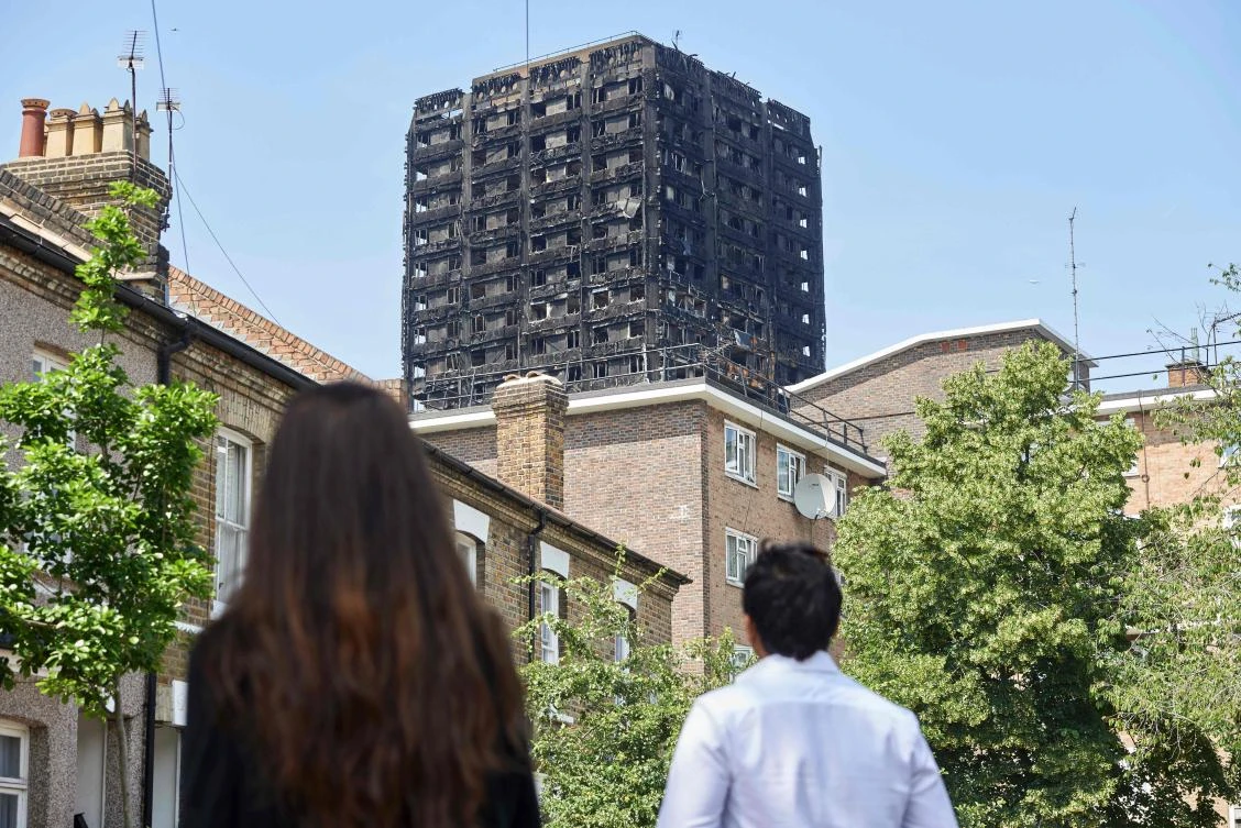 The burned-out shell of the Grenfell Tower block is seen behind terraced houses as local residents look on near the scene of the fire in North Kensington, west London. (AFP)