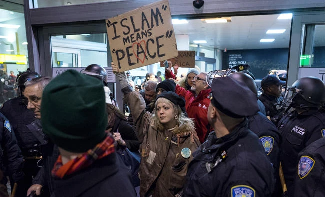 In this Jan. 28, 2017 photo, protesters are surrounded by police officers and travelers as they pass through an exit of Terminal 4 at John F. Kennedy International Airport in New York, after earlier in the day two Iraqi refugees were detained while trying to enter the country. US Customs and Border Protection officers will be key players in putting President Donald Trump's revised travel ban into effect on Thursday affecting visitors from six mostly Muslim countries. (AP Photo/Craig Ruttle, File)
