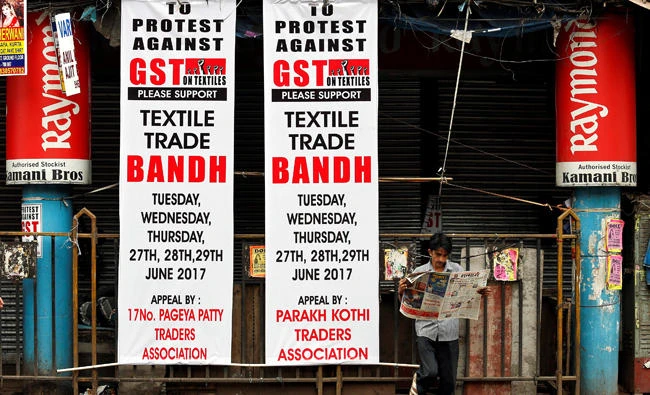 A man reads a newspaper next to banners in front of a closed garments market during a protest against the implementation of the Goods and Services Tax (GST) on textiles, in Kolkata, India. (Reuters)