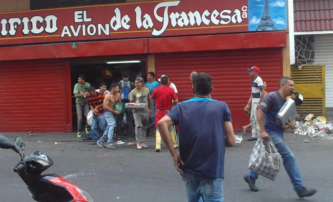 People running off with meat from a butcher shop in Turmero, Aragua state, near Maracay on Wednesday. Dozens of supermarkets, pharmacies and stores were looted and several government offices burned during the incident, following anti-government protests. (AP)