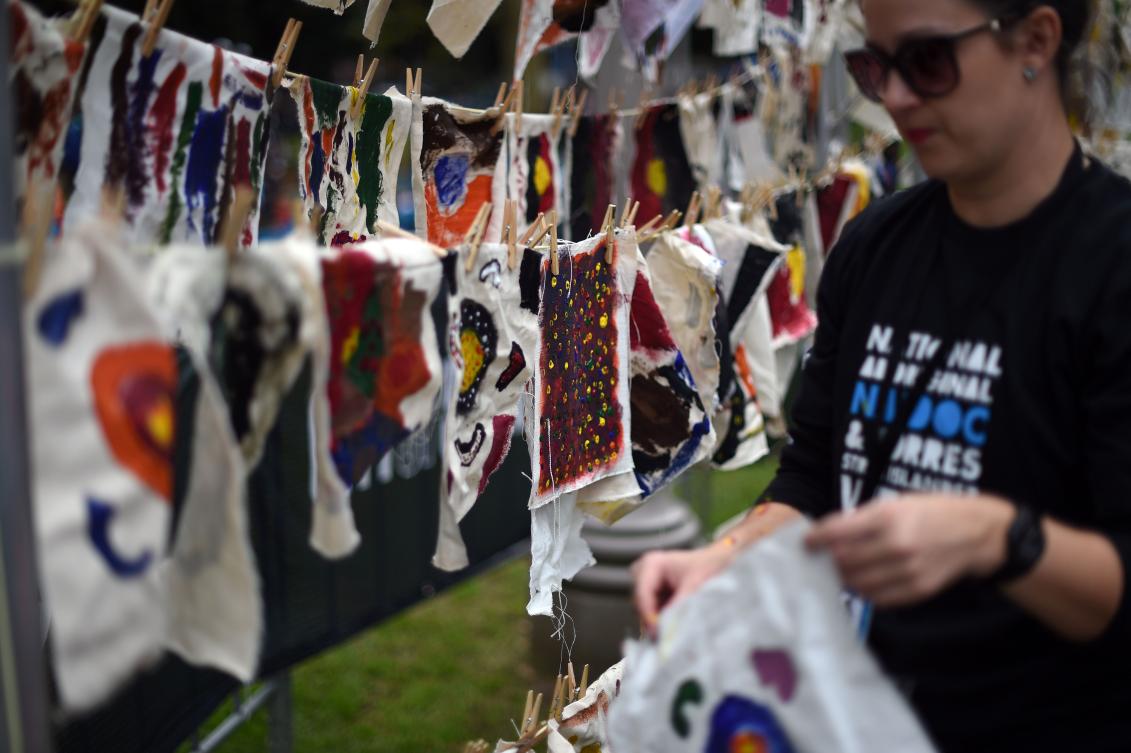 A volunteer hangs traditional Aboriginal art, painted by school children, up to dry at Sydney's Hyde Park on July 3, 2017. The week long annual event, with the theme of 'our languages matter', celebrates Aboriginal and Torres Strait Islander culture and takes place from July 3 in Hyde Park. / AFP / SAEED KHAN
