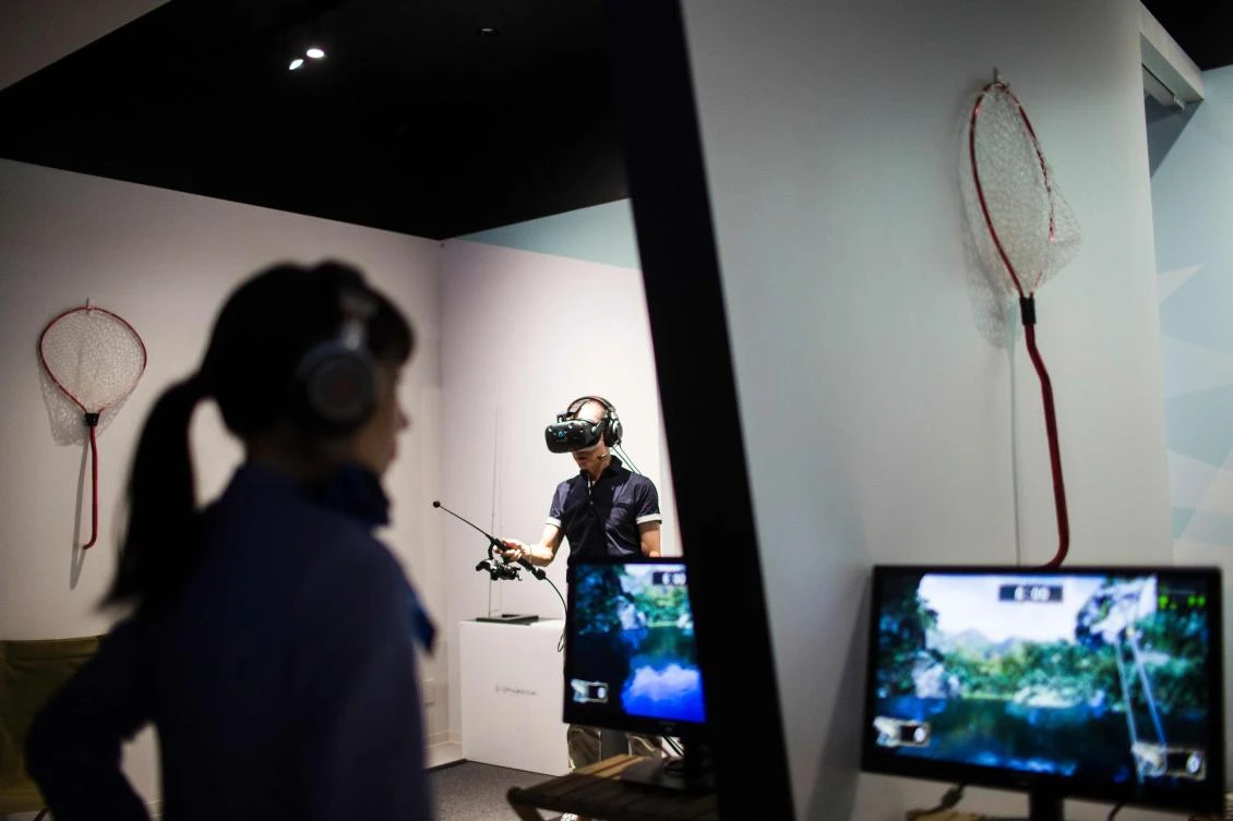An operator (L) looks at the screens as a man plays a virtual reality (VR) fishing game at the Bandai Namco game facility of VR Zone Shinjuku in Tokyo on July 22, 2017. / AFP / Behrouz MEHRI