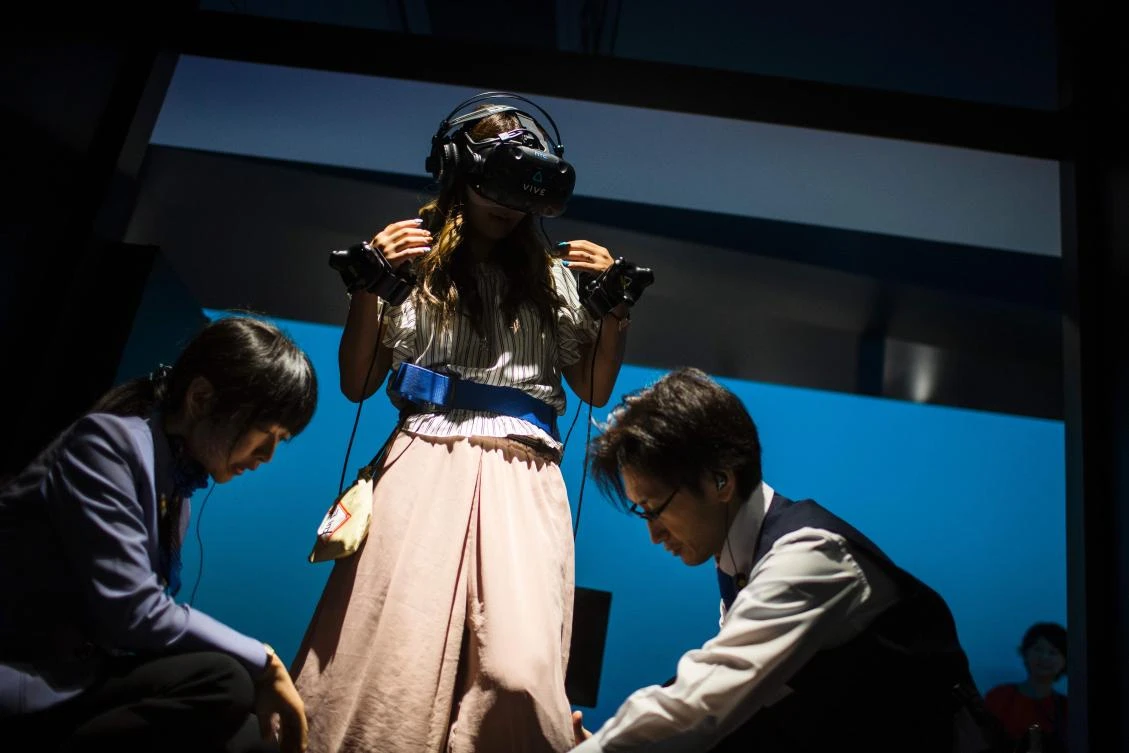 Employees of the Bandai Namco game company help a woman prepare to play a virtual reality (VR) Dragon Ball game at VR Zone Shinjuku in Tokyo on July 22, 2017. / AFP / Behrouz MEHRI