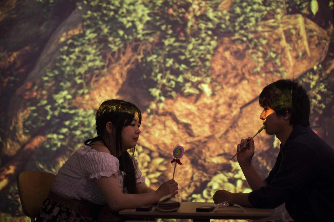 A couple sit in a cafe with a projection mapping installation background at the Bandai Namco game facility of VR Zone Shinjuku in Tokyo on July 22, 2017. / AFP / Behrouz MEHRI