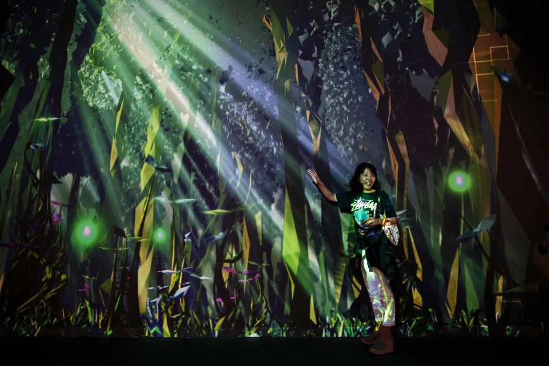 A woman poses next to a projection mapping touch reactive installation at the Bandai Namco game facility of VR Zone Shinjuku in Tokyo on July 22, 2017. / AFP / Behrouz MEHRI