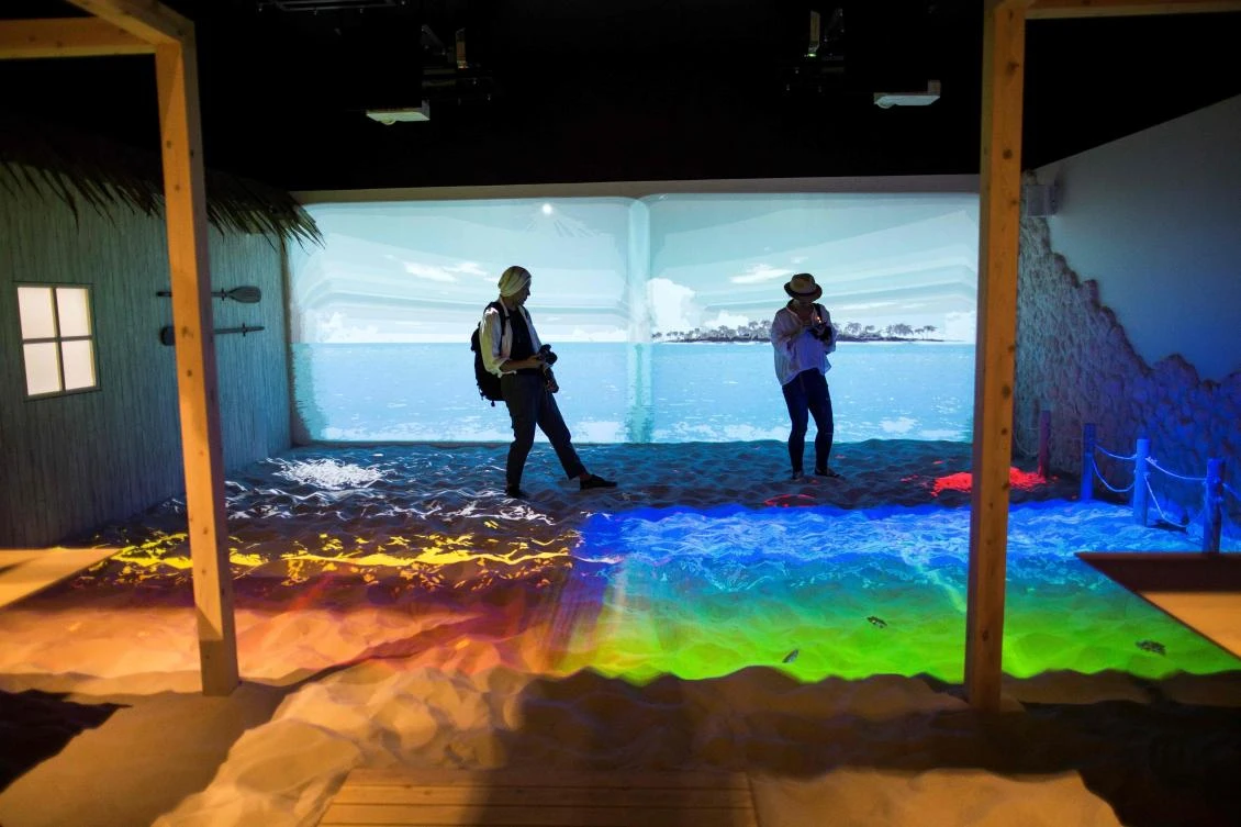 People walk around a beach simulation projection mapping installation at the Bandai Namco game facility of VR Zone Shinjuku in Tokyo on July 22, 2017. / AFP / Behrouz MEHRI