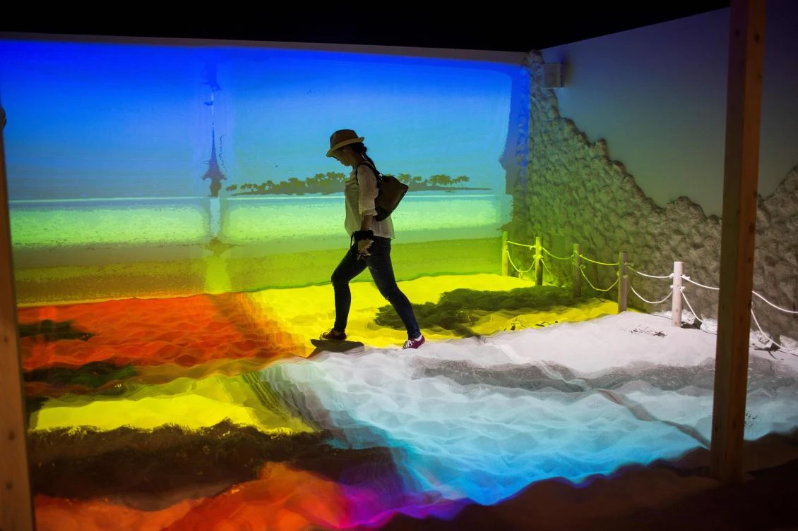 A woman walks around a beach simulation projection mapping installation at the Bandai Namco game facility of VR Zone Shinjuku in Tokyo on July 22, 2017. / AFP / Behrouz MEHRI