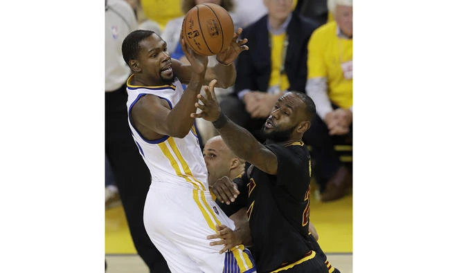 In this June 12, 2017, photo, Golden State Warriors forward Kevin Durant, left, passes against Cleveland Cavaliers forward LeBron James during Game 5 of basketball's NBA Finals in Oakland, California. (AP Photo/Marcio Jose Sanchez)