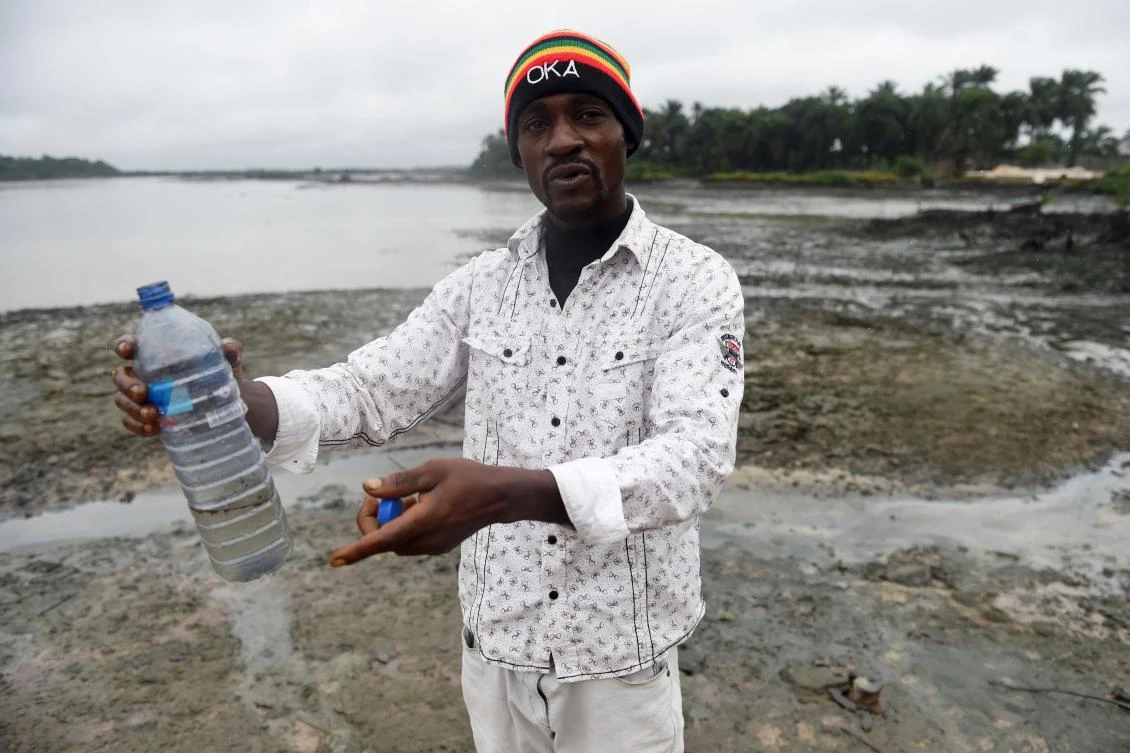 A fisherman holds a plastic bottle with water comming from the polluted Bodo River in Bodo, in the Gokana district of Ogoniland, southeast Nigeria. (AFP)