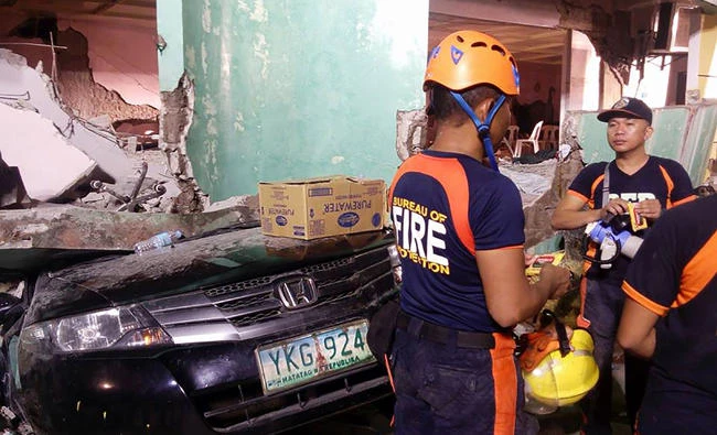 Rescuers stand next to a car buried under the rubble of a destroyed building after a 6.5-magnitude earthquake hit the town of Kananga, Leyte province, in central Philippines, on Thursday. (AFP / LITO BAGUNAS)