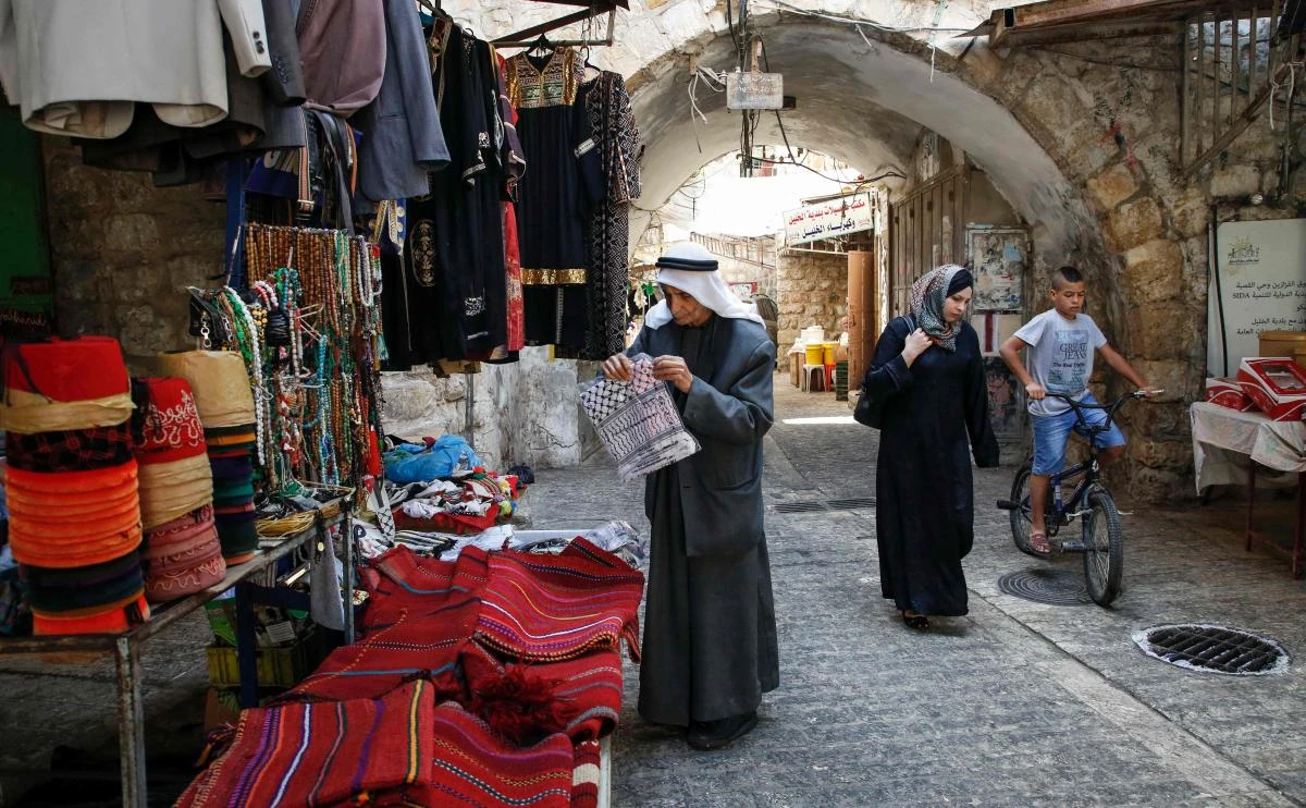 A Palestinian man browses merchandise as another woman walks by in an alley in the old market of the divided West Bank city of Hebron on July 7, 2017. (AFP)