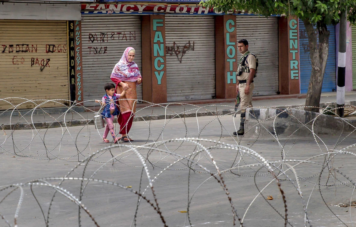 An Indian paramilitary force officer watches as a Kashmiri woman along with her child walks past a barbed-wire road checkpoint set up by Indian security forces in Srinagar, Indian controlled Kashmir, Friday, July 7, 2017. Government forces imposed curfew-like restrictions in many parts of Indian controlled Kashmir to stop anti Indian protests ahead of the first death anniversary of rebel leader Burhan Wani on Saturday. His killing by security forces last year sparked violent street clashes and almost daily protests throughout the region. (AP)