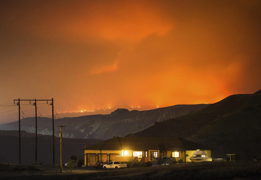 A wildfire burns on a mountain in the distance east of Cache Creek behind a house in Boston Flats, British Columbia, early Monday, July 10, 2017. (Darryl Dyck/The Canadian Press via AP)