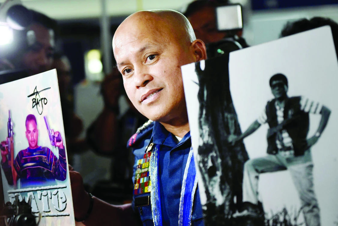 Philippine National Police chief Ronald Dela Rosa poses between a photo of himself and President Rodrigo Duterte at a gun show show in Manila on Thursday. (Reuters)
