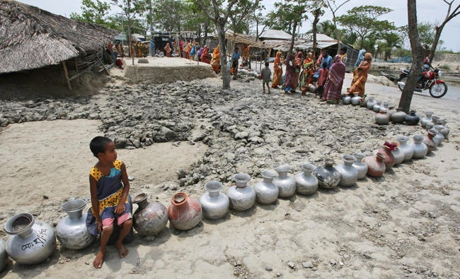 In this photo taken on May 14, 2010, A village girl sits on a vessel as she waits with others in a queue for water supplied by tankers at an area affected by last year's cyclone Aila in Nildumur, Satkhira district, southwest of the capital Dhaka, Bangladesh. A report by the Asia Development Bank on Friday says Asia will endure extreme heat, rising sea levels, growing losses from severe weather and increasing food insecurity in coming decades as climate change raises temperatures and alters weather patterns across the globe. (AP Photo/Pavel Rahman, File)
