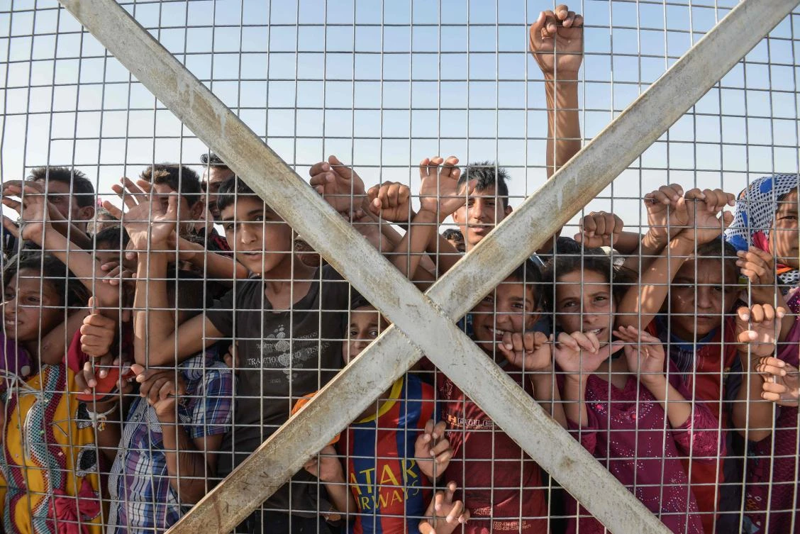 (FILES) This file photo taken on June 10, 2017 shows displaced Iraqi children gathering behind a fence at the Hasan Sham camp for internally displaced people on June 10, 2017. The unprecedented destruction in the country's second city and the unstable security situation will delay the return home of hundreds of thousands of people who fled. (AFP)