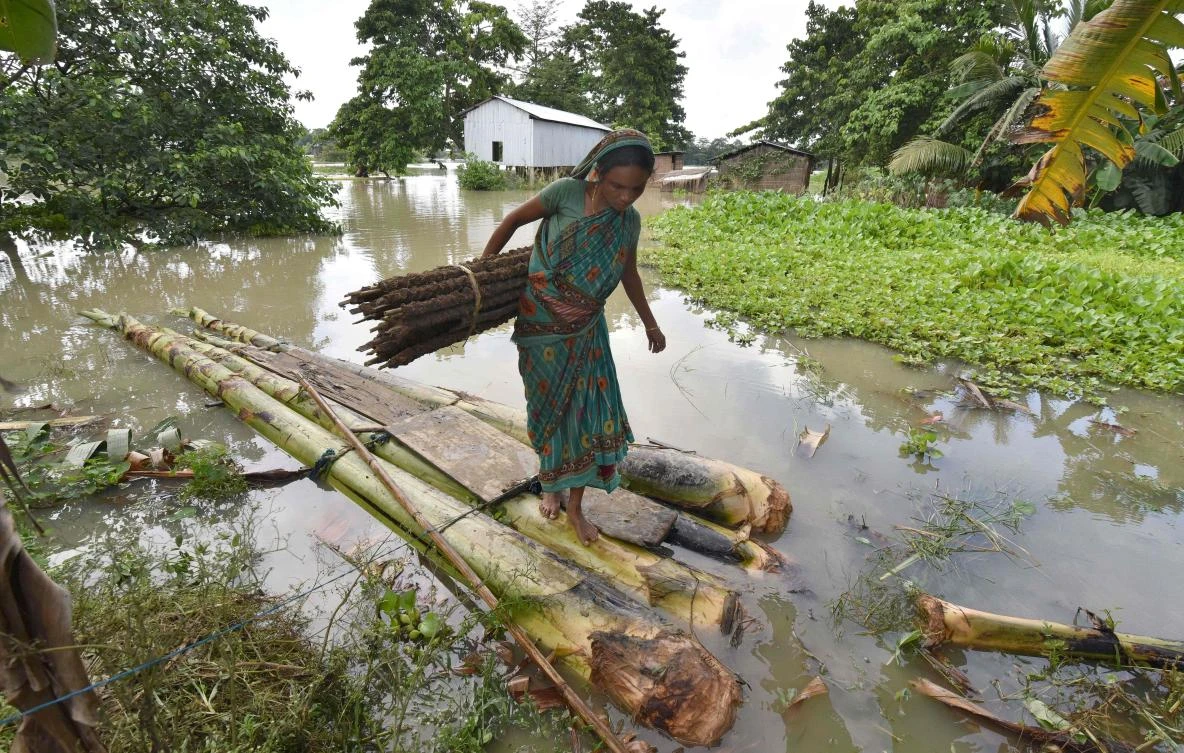 (FILES) In this photograph taken on July 5, 2017, an Indian woman carries cow dung, which is used as fuel for fires, on a raft through floodwaters in Buraburi village in Morigoan district in the northeastern state of Assam. At least five people were killed and 10 missing July 11 after a massive landslide buried homes in a remote village in northeast India, a disaster management official said. An avalanche of mud and rock struck the village after weeks of heavy rain in Papum Pare district in the Himalayan state of Arunachal Pradesh along the border with China. (AFP)