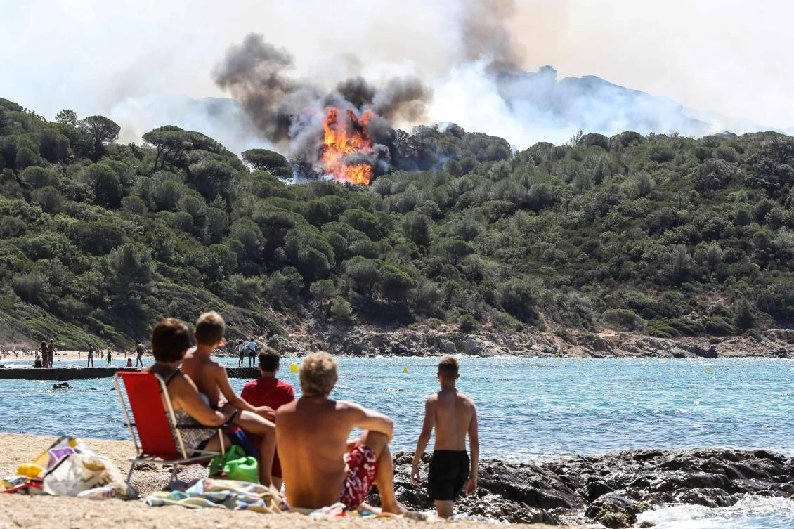 People enjoy the beach as they look at a forest fire in La Croix-Valmer, near Saint-Tropez, on July 25, 2017. Firefighters battle blazes that have consumed swathes of land in southeastern France for a second day, with one inferno out of control near the chic resort of Saint-Tropez, emergency services say. (AFP)