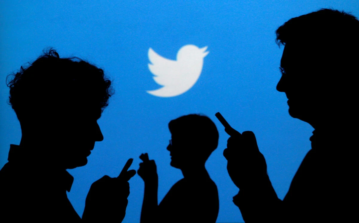 People holding mobile phones are silhouetted against a backdrop projected with the Twitter logo. (Reuters)