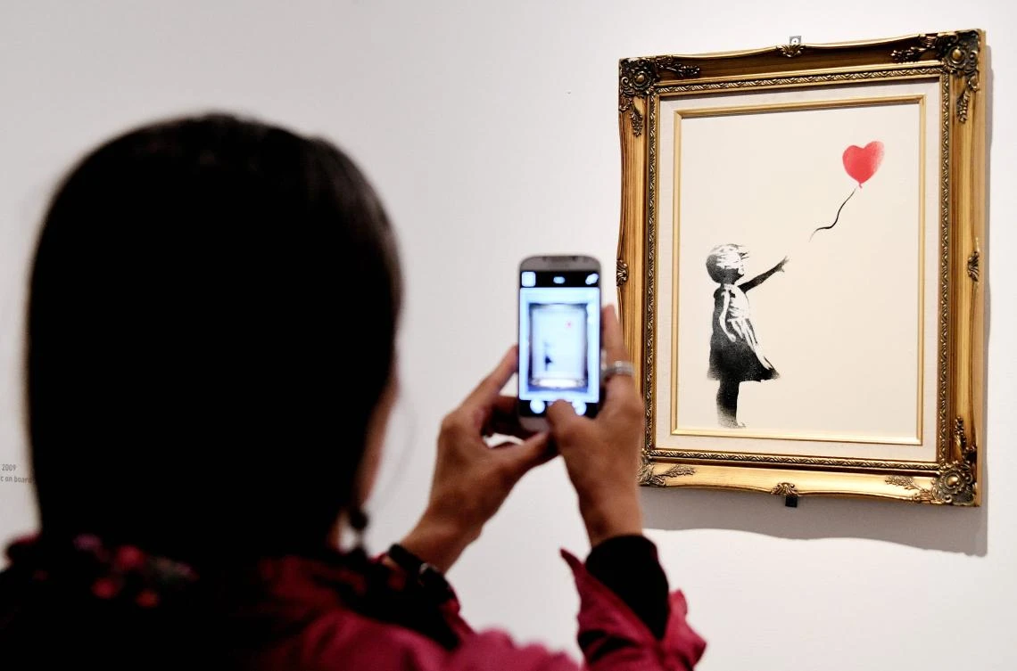 This file photo taken on May 23, 2016 shows a woman takes picture on May 23, 2016, of a piece entitled “Girl with ballon, red” by England-based graffiti artist Banksy in Rome’s Palazzo Cipolla. (AFP)