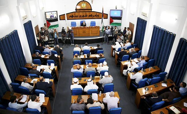 Lawmakers from Hamas and Fatah, affiliated with exiled former Gaza strongman Mohammed Dahlan, wait for his speech via video conference from his office in the United Arab Emirates, during the first meeting together at the Gaza's parliament building in Gaza City, on Thursday. (AP)