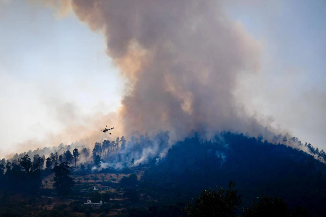 A fire-fighting helicopter flies over a wildfire near Vila Velha de Rodao, central Portugal, on July 27, 2017. Forest fires raged in the early hours of Thursday in central Portugal, cutting off roads and forcing thousands to flee just a month after deadly blazes left more than 60 people dead. (AFP)