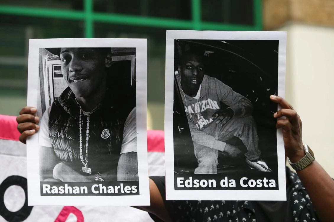 A protester holds up printed photographs of Edir (Edson) Da Costa (R), a 25-year-old man who died in hospital after being detained by police in London, and Rashan Charles (L), a 20-year-old whose death after being followed by police last week into a convenience store and allegedly apprehended has caused anger in the local community, during a vigil for Rashan outside Stoke Newington police station in east London on July 29, 2017. (AFP)