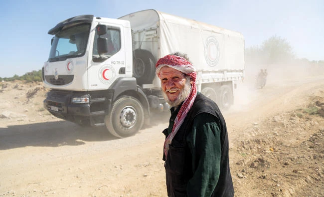 A Syrian man smiles as UN and Syrian Arab Red Crescent (SARC) convoy trucks arrive in the town of Nashabiyah in eastern Ghouta on Sunday to deliver aid packages for the first time in five years. (AFP)
