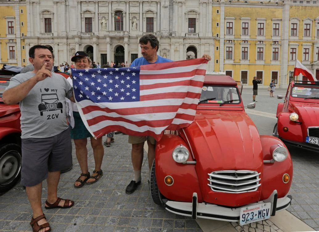 US participants hold a flag after their arrival to the parking area in Mafra after the parade of Citroen classic cars 2CV during the World 2017 2CV Meeting July 30, 2017. The event is held between the 26th and the 31st of July 2017, 30 years after Portugal hosted the seventh 2CV World Meeting in 1987, and will include activities ranging from an open air fair, a competition to disassemble and reassemble, an "elegance" contest for original and modofied 2CV's, a chimes concert, to a short term 2CV museum hosted by the Marfa national palace featuring vehicles from the Citroen Heritage collection purposely brought from Paris. / AFP / JOSE MANUEL RIBEIRO
