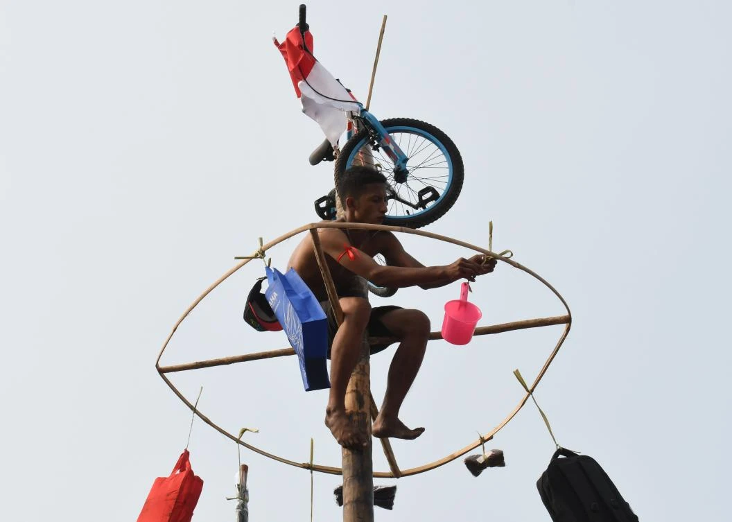 A participant collects a prize after making it to the top in Panjat Pinang, a pole climbing contest, as part of festivities marking Indonesia's 72nd Independence Day on Ancol beach in Jakarta on August 17, 2017. Panjat Pinang, a tradition dating back to the Dutch colonial days, is one of the most popular traditions for celebrating Indonesia's Independence Day. / AFP / GOH Chai Hin