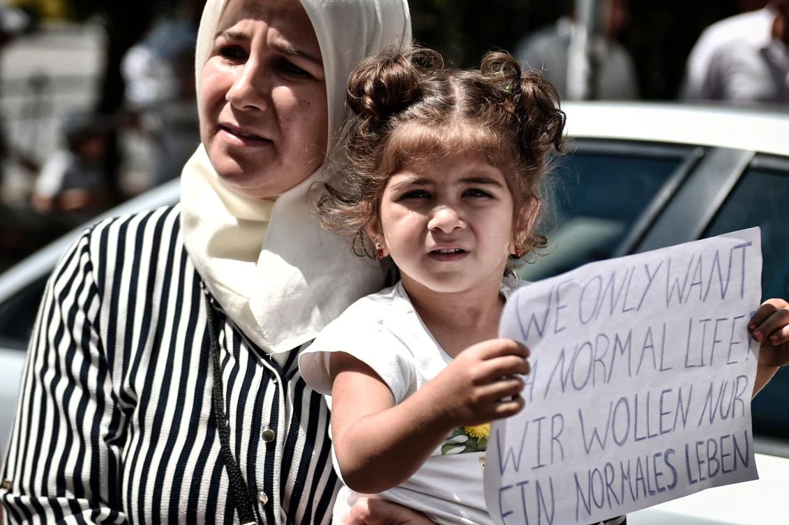 A Syrian girl holds a placard reading in English and German 'We only want a normal life' outside the German embassy in Athens on July 19, 2017 during a protest of Syrian refugees against delays in the reunification process with their families in Germany. The German government has significantly cut back on family reunions for refugees arriving from Greece since May 2017. Asylum seekers - mostly Syrian refugees in Greece's case - are entitled to join family members elsewhere in the European Union within six months from the date their request is approved. / AFP / LOUISA GOULIAMAKI