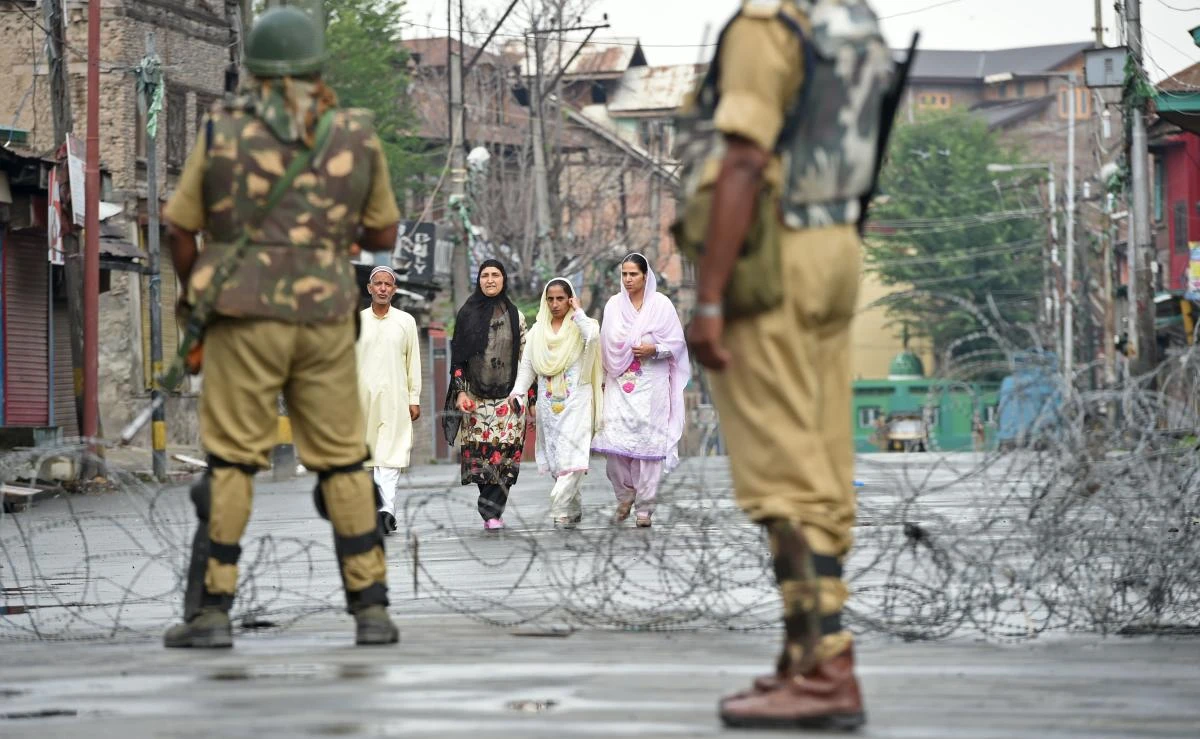 Indian paramilitary troopers stand guard as Kashmiri pedestrians walk along a road during restrictions after Kashmiri seperatists called for a one-day strike to protest a civilian killing in Srinagar on August 2, 2017. Thousands of Indian soldiers enforced a lockdown August 2 in parts of Kashmir, fearing violent reprisals a day after a top militant commander and two civilians were killed in clashes in the disputed Himalayan territory. Residents in the old quarters of Srinagar, the main city in Indian-administered Kashmir, were ordered to stay indoors and obey the curfew as thousands of riot police patrolled streets lined with steel barriers and razor wire. / AFP / TAUSEEF MUSTAFA
