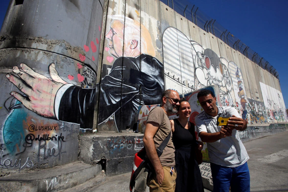 Tourists stand in front of a grafitti depicting U.S President Donald Trump on the controversial Israeli barrier in the West Bank town of Bethlehem August 4, 2017. (REUTERS)