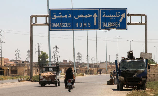 A photo taken on August 3, 2017 shows vehicles driving past a road sign that says "Talbiseh" in the eponymous central Syrian rebel-held town, north of Homs, along the highway between the capital Damascus and the central city of Homs. (AFP)