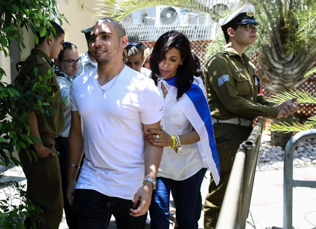 Israeli soldier Elor Azaria (C-L), who shot dead a wounded Palestinian assailant in March 2016, is escorted by his mother Oshra (C) while she is draped in an Israeli flag, to attend a hearing at a military court in Tel Aviv on July 30, 2017. Judges rejected an appeal by Azaria, the Israeli sergeant and military medic at the time of the incident, who was convicted of manslaughter and sentenced to 18 months in prison for shooting dead a prone Palestinian assailant, Israeli media reports said. The reports said military judges also rejected an appeal by prosecutors to increase his sentence. / AFP / AP / AP / Dan Balilty