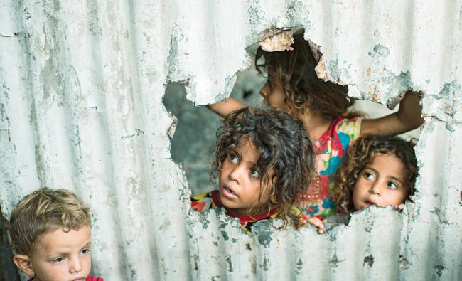 Palestinian children look through a hole in a sheet metal fence outside their home in Gaza City on Tuesday. (AFP)