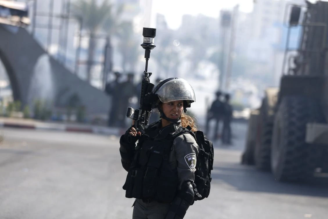 An Israeli security forces member flashes her weapon during clashes with Palestinian protestors near the Jewish settlement of Beit El, on the outskirts of the West Bank city of Ramallah, on July 28, 2017, as protests erupt in support of the Al-Aqsa mosque compound after Israeli police barred men under 50 from Friday prayers in the Old City of Jerusalem. Palestinians held mass prayers outside of a sensitive Jerusalem holy site after Israeli police barred men under 50 from entering following two weeks of tensions and deadly unrest. Despite fears of violent clashes around the Haram al-Sharif compound, known to Jews as the Temple Mount, the area was largely calm following Friday's midday prayers. (AFP)